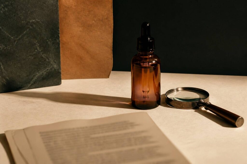 Flacon de cosmétique en verre ambré posé sur un fond kraft écru avec une loupe à proximité